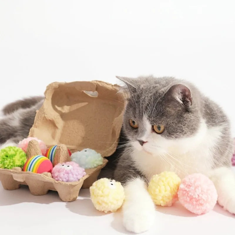 Cat lying beside egg-shaped yarn balls in box