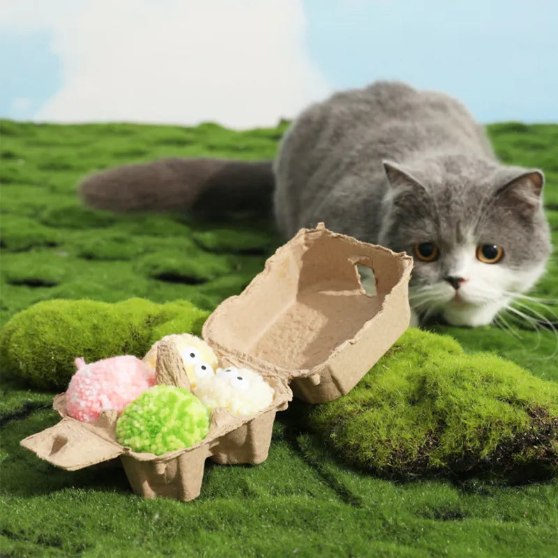 Cat lying on grass beside egg-shaped yarn balls