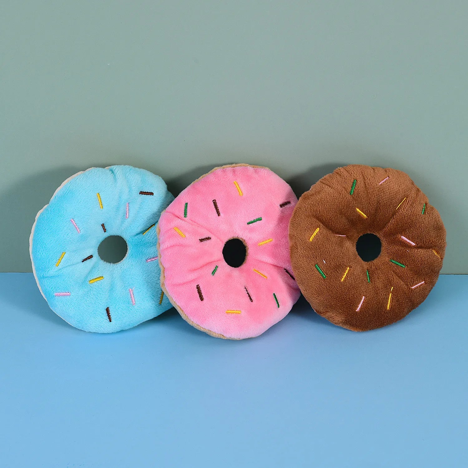 Three plush donut toys for dogs in blue, pink, and brown