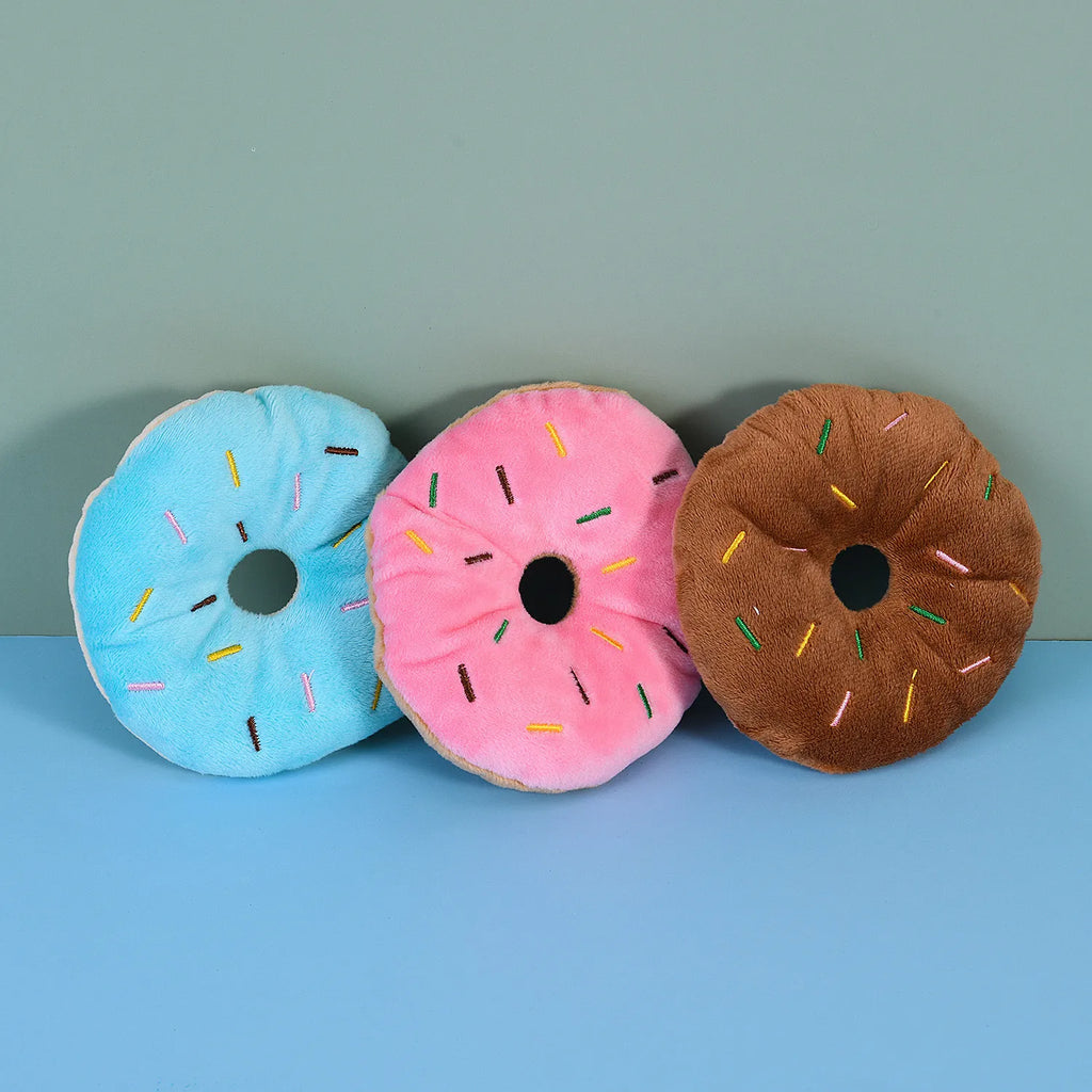 Three plush donut toys for dogs in blue, pink, and brown
